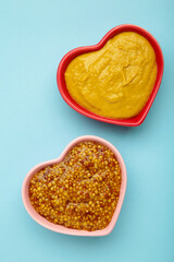 Dijon mustard with french mustard on heart shaped bowl on blue background.