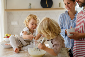 Young nuclear family making pancakes together. Parents and children in kitchen, preparing pancake batter, spending weekend day indoors.