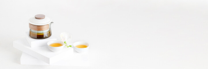 Contemporary tea ceremony concept, minimalist crystal teapot and white bowls on the podium banner...