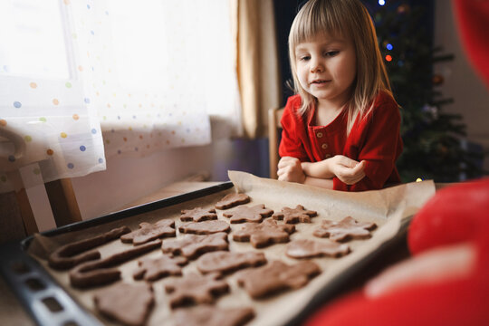 Cute girl looking at homemade Christmas cookies on baking sheet