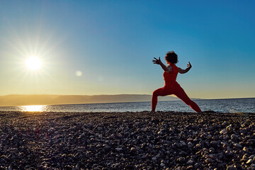 Athletic woman practicing yoga at beach during sunrise in Sicily