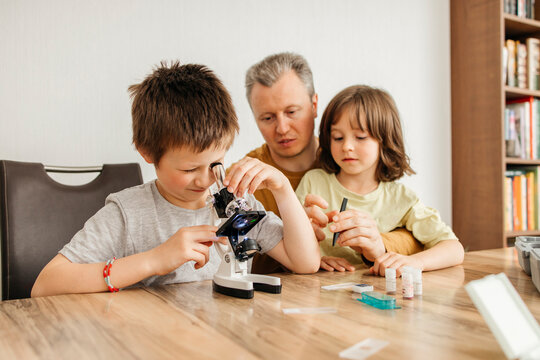 Boy looking through microscope and sitting with father and sister at home