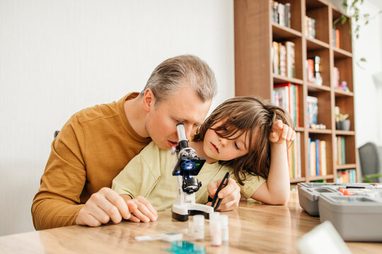 Curious man looking through microscope and sitting with daughter at home