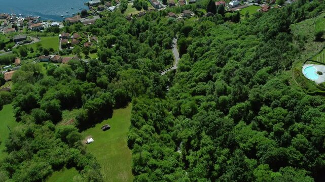 Flying over green trees and quaint town on shore of scenic Lake Orta, Italy
