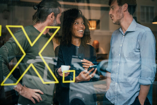 Happy business colleagues talking with each other in cafe seen through window
