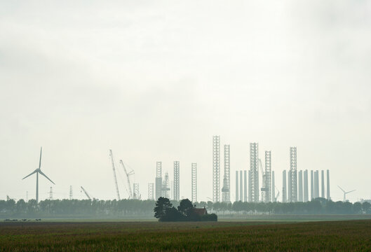 Wind turbines with oil drilling rigs under sky at Vlissingen harbor in Netherlands