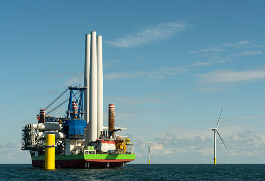 Crane vessel ship constructing offshore wind turbine farm in sea under cloudy sky
