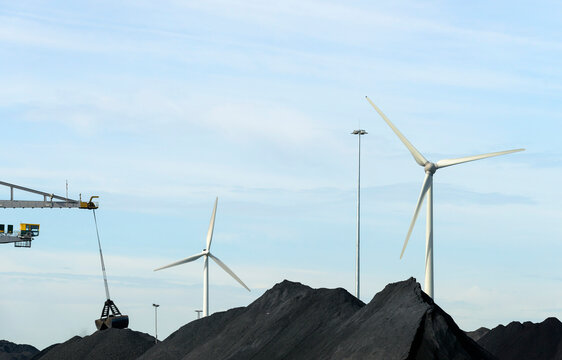 Heap of coal near wind turbines under blue sky