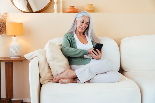 Happy mature woman using mobile phone on sofa at home