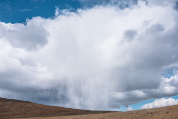 Alpine view to giant white cloud pours rain in large mountains. Awesome huge low cloud with rain poured down above high stone pass. Dramatic mountain landscape with big unusual rainy cloud in blue sky