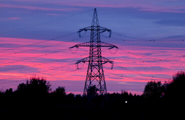 Fototapeta premium Silhouetted High Voltage Towers Against a Stunningly Vibrant Pink and Purple Sunset Sky