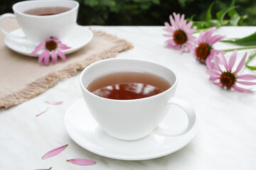 Cups of healthy echinacea tea, coneflower herbs and on a light table. Side view.