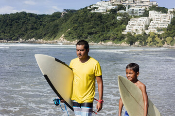 Latin father and son surfers holding surfboard on the beach in Acapulco Mexico. Hispanic people in summer sport activity