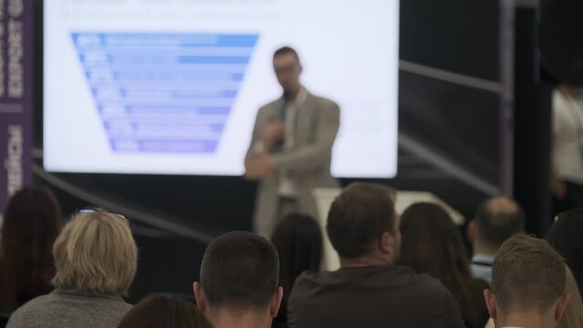 Business professional presenting to a diverse audience at a seminar. The focus is on a visual presentation, engaging attendees with relevant content.