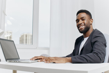 Focused african american man working on laptop at modern office desk with notebooks and coffee mug