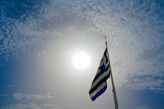 Greek Flag on top of the Acropolis of Athens against the backdrop of the sun.