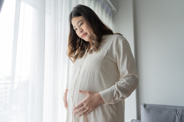 Pregnant asian woman holds hands on belly touching her baby caring about her health Beautiful happy pregnant woman tender mood photo of pregnancy