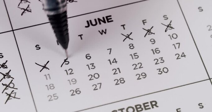Close-up of a black pen pointing at dates on a June calendar with some days crossed out, indicating organization and planning. Black Pen Pointing at Calendar Dates in June with Crossed Out Days