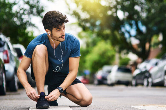 Fitness, man and tying shoelace in road, exercise and workout or safety preparation in street with morning routine. Earphones, audio tech and streaming motivation or music, runner and athlete outside