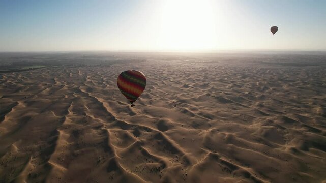 Drone flies around balloons with tourists over the sand dunes of the desert in Dubai
