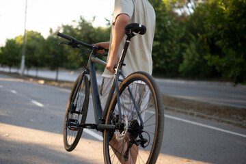 Fototapeta premium man walks on a paved path in a park, carrying a black bicycle over his shoulder