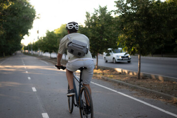 bicycle courier rides on a bike path in the city, wearing a helmet and carrying a small delivery bag