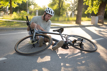man wearing a helmet sits on the asphalt of a city street, his leg injured, after a bicycle crash