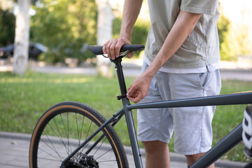 Naklejka premium man in a light-colored shirt adjusts the seat height of his bicycle. He is standing outside on a sunny day