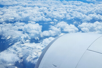 Aerial View of Snow-Capped Mountains and Fluffy Clouds from Airplane Window