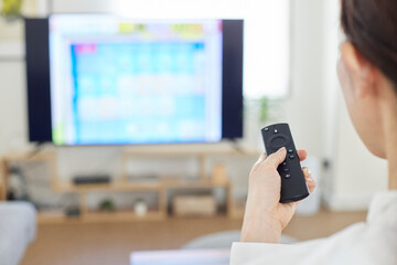 リビングにて動画配信サービスを楽しむ日本人女性の手元とリモコン