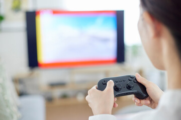 リビングにてオンラインゲームを楽しむ日本人女性の手元とコントローラー