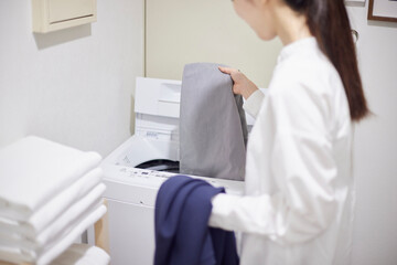 脱衣所にて洗濯機に洗濯物の衣類を入れる日本人女性の手元
