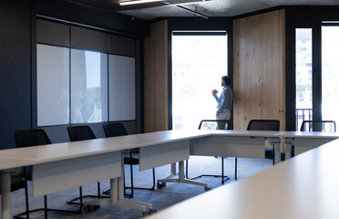 Businessman standing by window in modern office, holding baby and working, copy space