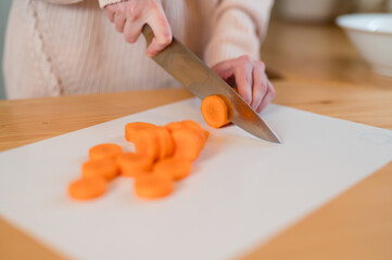 Pieces of carrot on a cutting board  with girl hands cutting carrot in background