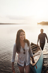 Fototapeta premium Sunset, boat and teamwork with couple in lake for adventure, summer and journey in nature. Man, woman and sunshine or wellness for travel, freedom and support or canoe in water by river or creek