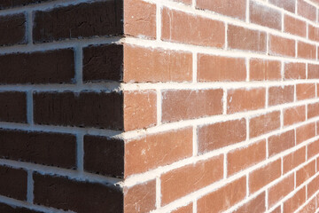 Corner of a brick house. One wall is illuminated by sunlight, the other is in shadow. Close-up. Background.