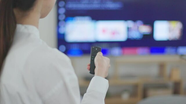 リビングにて動画配信サービスを楽しむ日本人女性の手元とリモコン