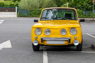 A bright yellow vintage car with classic round headlights is parked slightly crooked in an empty...