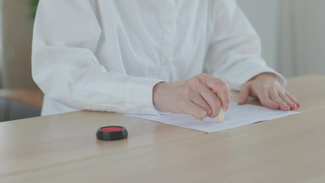リビングの机にて書類に捺印をする日本人女性