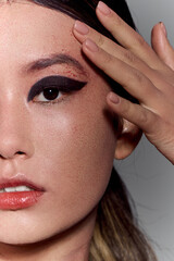 A close-up portrait of an Asian woman with bold eyeliner and nude nail polish.