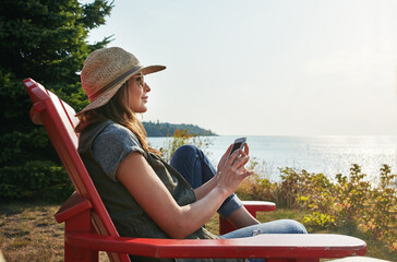Travel, relax and woman with mobile in nature for holiday, summer vacation or happiness. Outdoor, sunglasses and person on chair for weekend trip, comfortable or peaceful morning in Michigan