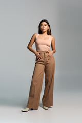 Fototapeta premium A woman in tan trousers and a pink top stands in a studio setting.