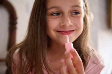 Young girl happily applying pink lip gloss at home