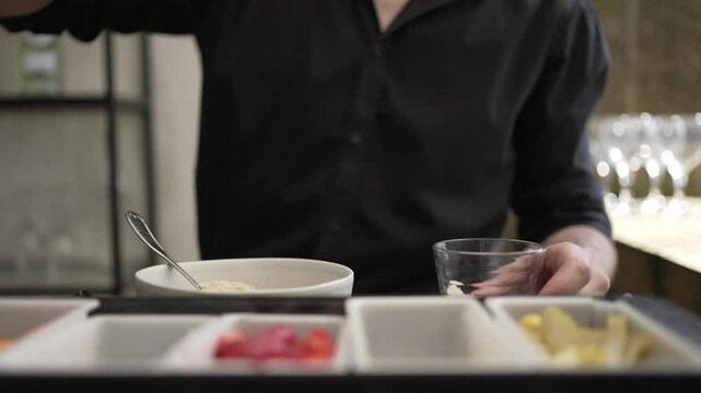 Bartender muddling ingredients in a glass with various garnishes on the bar counter.