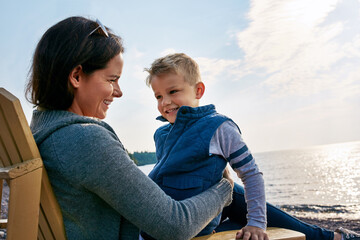 Obraz premium Beach, relax or smile with mom and son on chair by ocean for bonding, island holiday or travel together. Children, family or vacation with single parent woman and boy child outdoor by sea for love