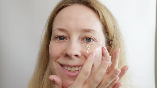 Woman putting eye patches on her face on white background, moisturizing gel pads, shiny facial mask, sparkle skin care.