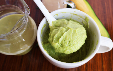 Scoop out the avocado pulp from a white ceramic bowl with a handle. Placed next to a glass jar of Mall Milk on a wooden table.

