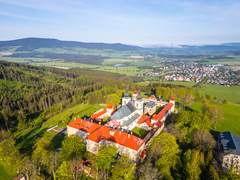 An aerial view of Hora Matky Bozi Monastery, located in Dolni Hedec near Kraliky, Czechia. The monastery is surrounded by lush greenery and a scenic landscape.