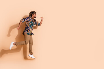 Obraz premium Full size photo of pretty young guy jump running wear trendy print outfit isolated on beige color background