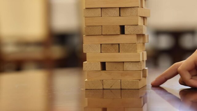 A person carefully removes a block from a tall stack of wooden blocks